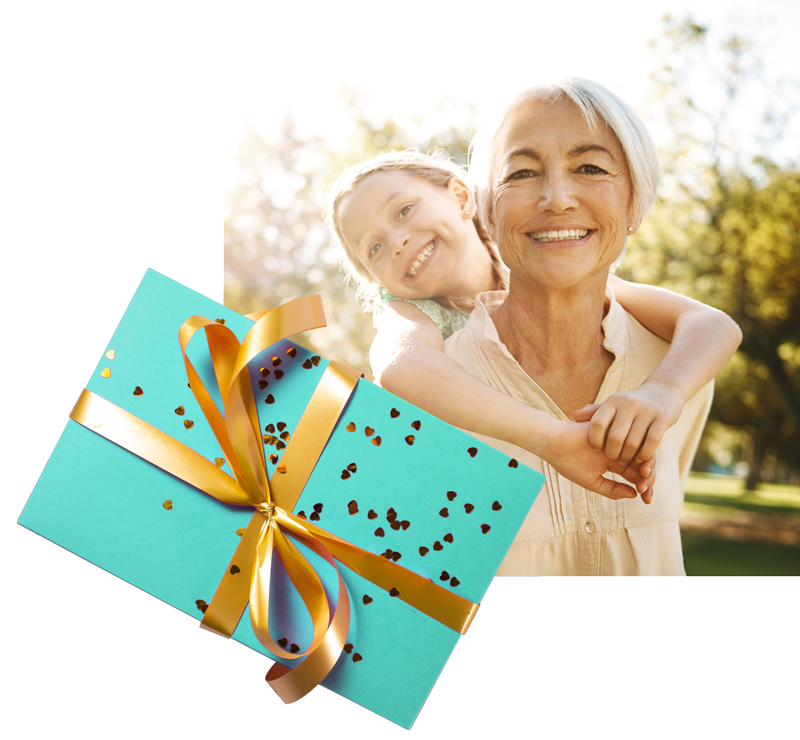 Geschenkbox mit Foto im Hintergrund - Frau trägt Enkelin auf dem Rücken und lächelt in die Kamera.